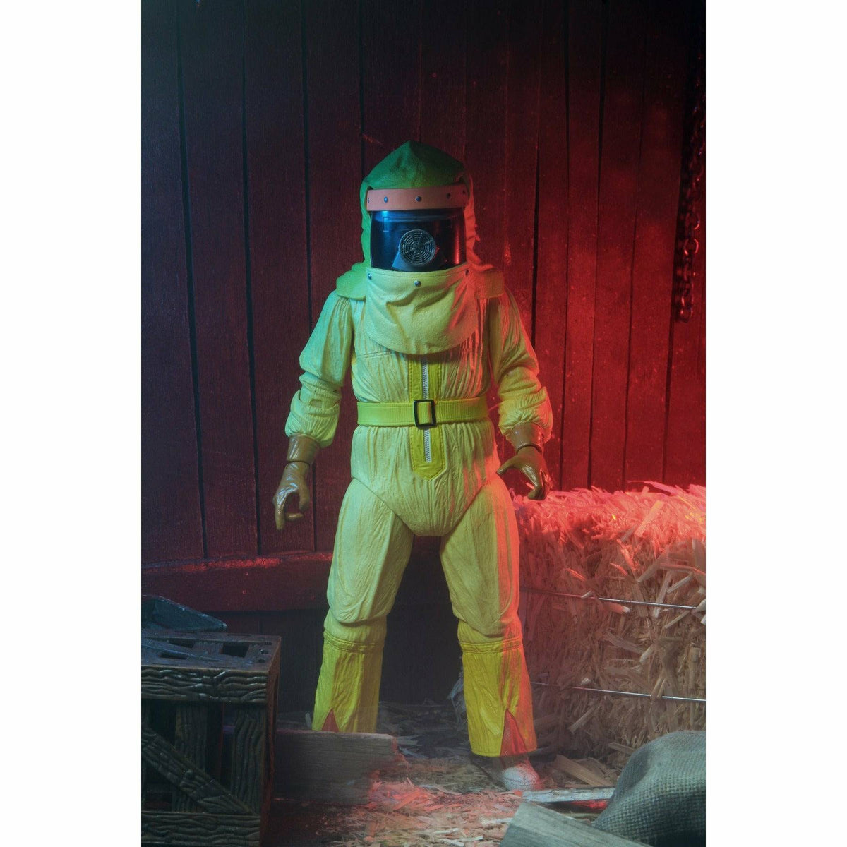 Person wearing a yellow hazmat suit and helmet in a dimly lit room with wooden walls and hay.