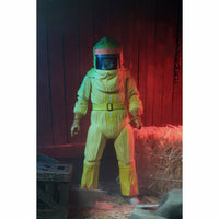 Person wearing a yellow hazmat suit and helmet in a dimly lit room with wooden walls and hay.