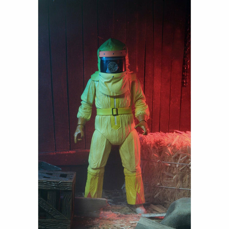 Person wearing a yellow hazmat suit and helmet in a dimly lit room with wooden walls and hay.