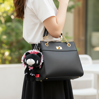 Black handbag with a plush toy attached, held by a person outdoors.