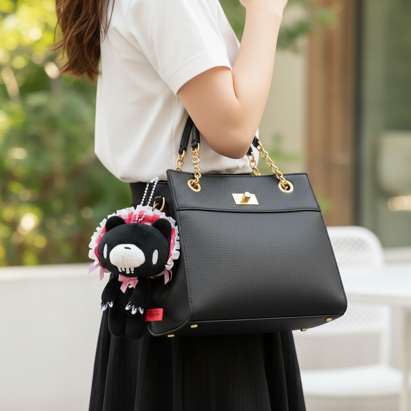 Black handbag with a plush toy attached, held by a person outdoors.