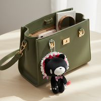Green handbag with a black and white plush toy keychain on a light wooden surface.