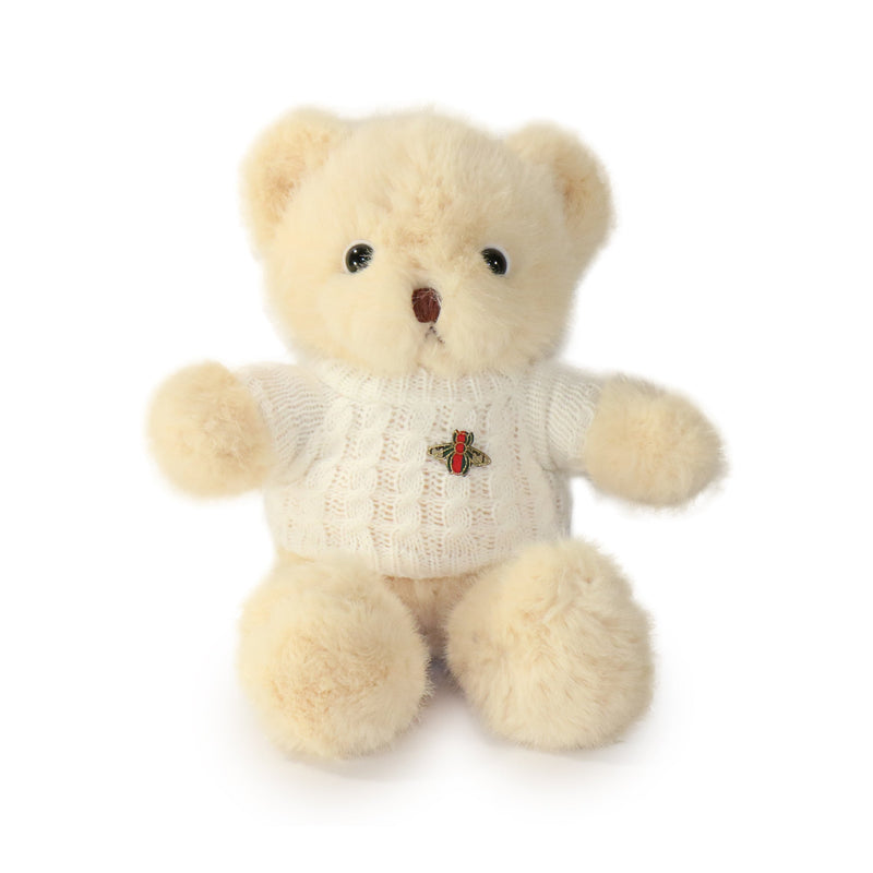 Beige teddy bear wearing a sweater with a brooch on a white background