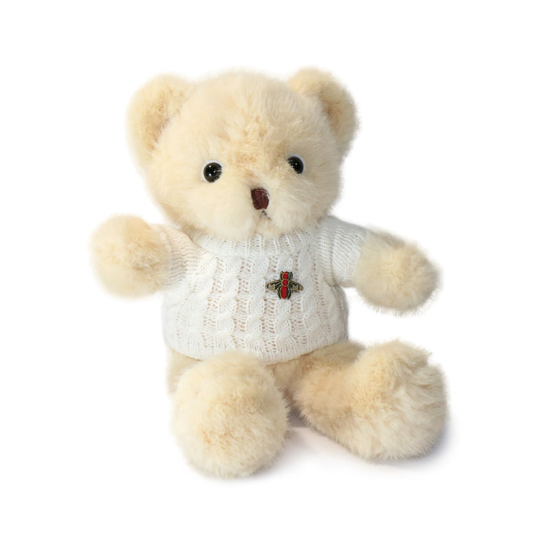 Beige teddy bear wearing a white sweater with a red bee emblem on a white background