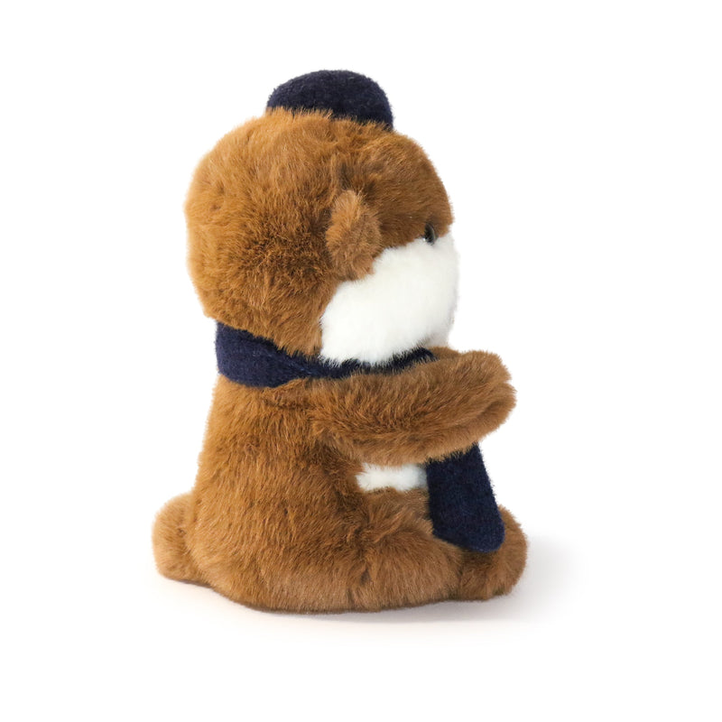 Plush toy resembling a marmet wearing a navy scarf and hat on a white background