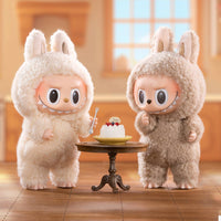 Two plush toys in bunny costumes standing next to a small table with a cake.