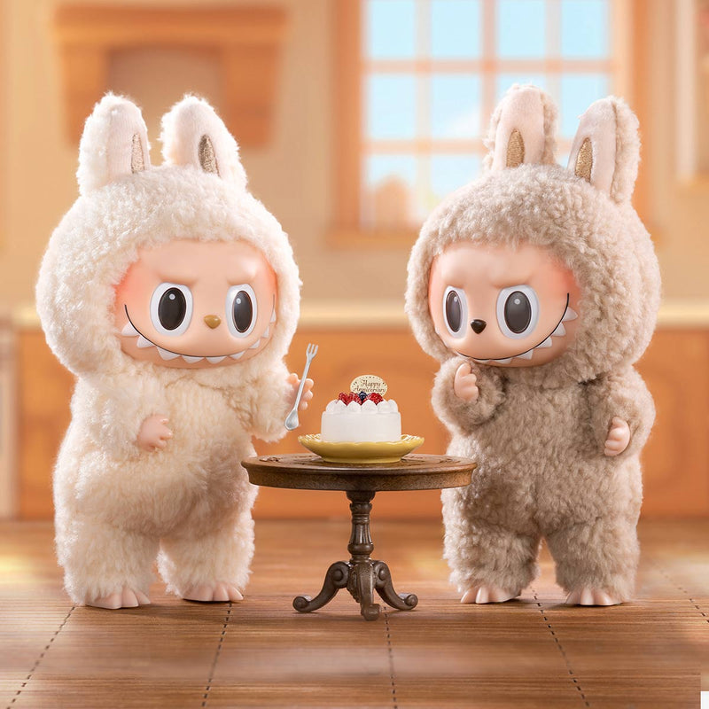 Two plush toys in bunny costumes standing next to a small table with a cake.
