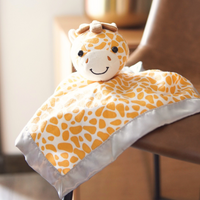 Giraffe-shaped soft toy with a patterned blanket on a wooden surface