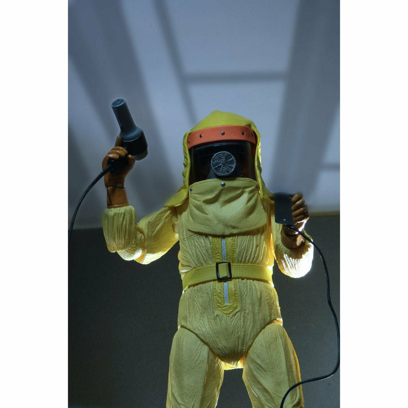 Person wearing a yellow hazmat suit holding two black devices against a white background