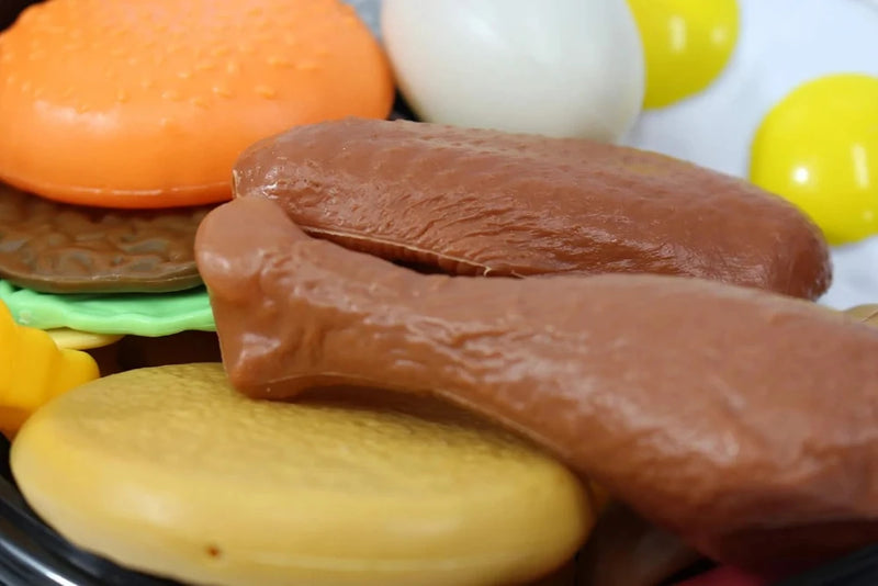 Close-up view of toy food including a plastic burger, chicken drumsticks, and sunny-side-up eggs for children's play kitchen.