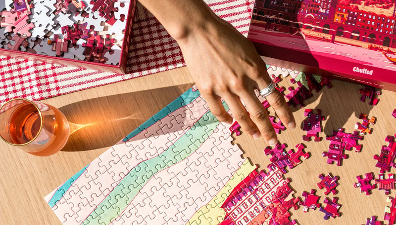 Person working on a puzzle with a glass of wine on a table