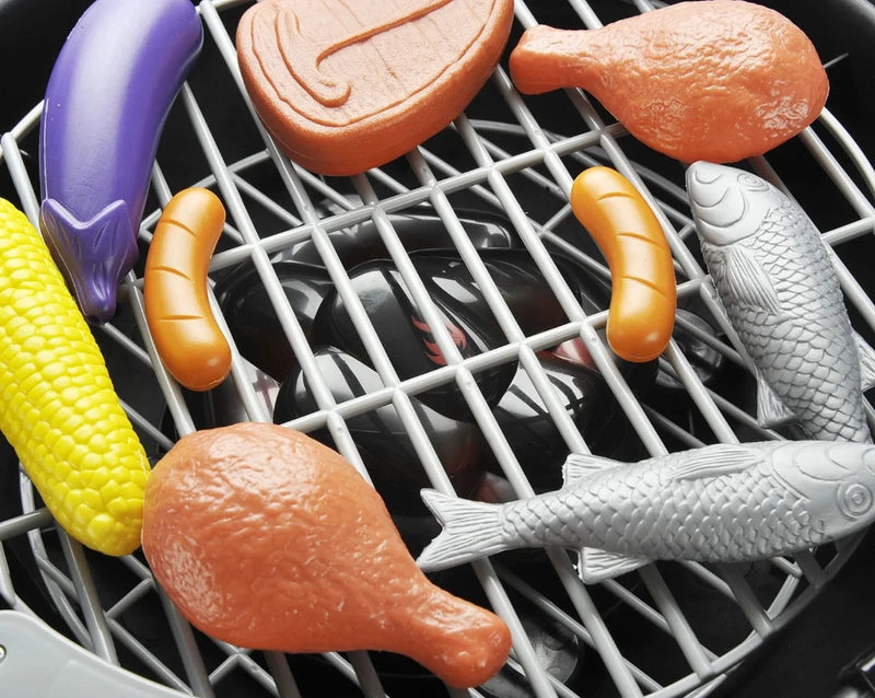 Assortment of realistic BBQ food toys on kids' grill, including drumstick, sausage, fish, and corn.